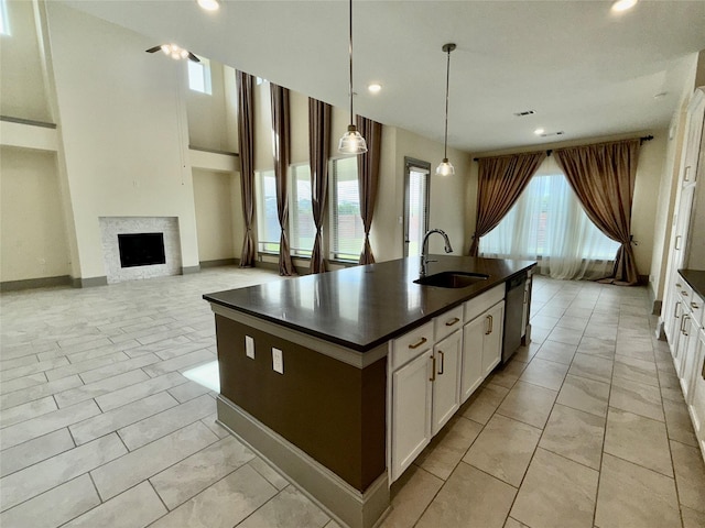 kitchen featuring stainless steel dishwasher, dark countertops, a kitchen island with sink, and a sink