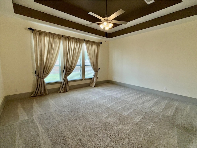 carpeted spare room with ceiling fan, a raised ceiling, and baseboards