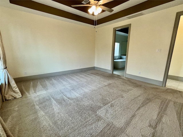 spare room with carpet flooring, a tray ceiling, a ceiling fan, visible vents, and baseboards