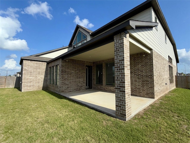 view of side of home with a lawn, fence, a patio area, and brick siding