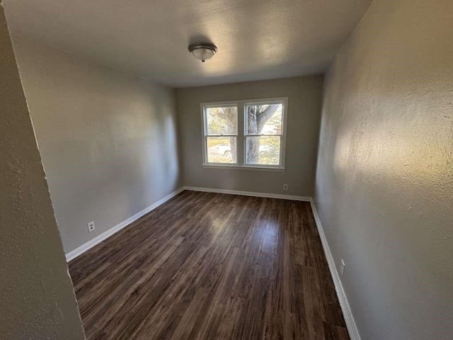 unfurnished room with dark wood-type flooring, a textured wall, and baseboards