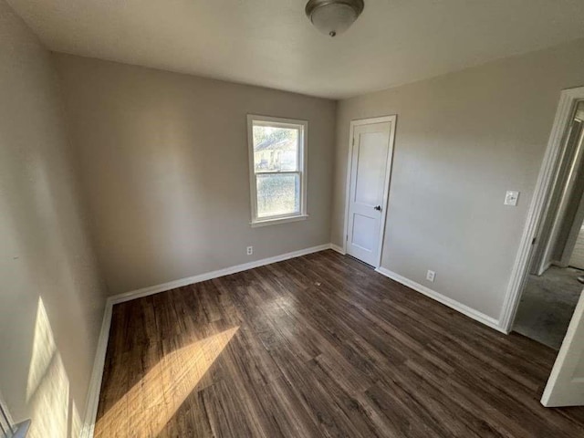 unfurnished bedroom with a closet, baseboards, and dark wood-type flooring