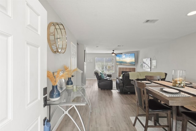 dining area featuring ceiling fan, a fireplace, a textured ceiling, and hardwood / wood-style floors