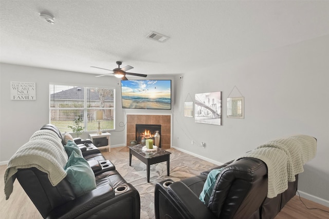 living room with ceiling fan, a textured ceiling, light hardwood / wood-style flooring, and a tiled fireplace