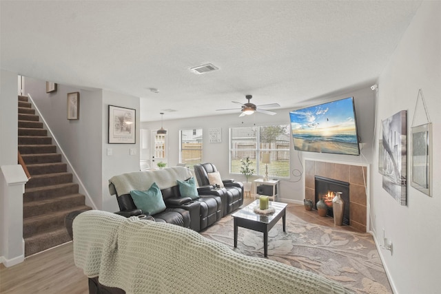 living room with a textured ceiling, ceiling fan, hardwood / wood-style floors, and a tile fireplace