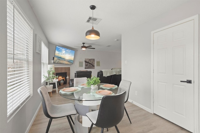 dining area featuring light wood-type flooring, ceiling fan, and a fireplace