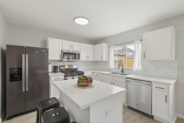 kitchen with appliances with stainless steel finishes, sink, white cabinets, a breakfast bar, and a center island