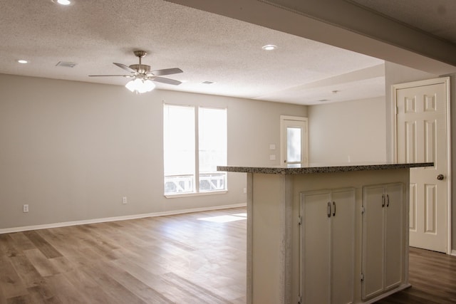 kitchen featuring ceiling fan, dark stone countertops, a center island, light wood-type flooring, and a textured ceiling