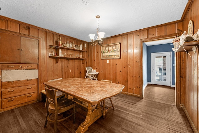 dining space featuring dark hardwood / wood-style flooring, wooden walls, a textured ceiling, and a notable chandelier