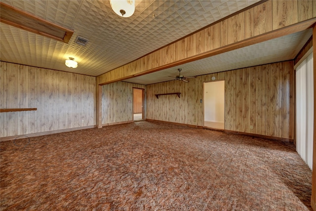 carpeted empty room with ceiling fan and wood walls