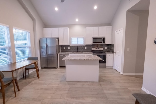 kitchen featuring white cabinetry, stainless steel appliances, light stone counters, and a center island