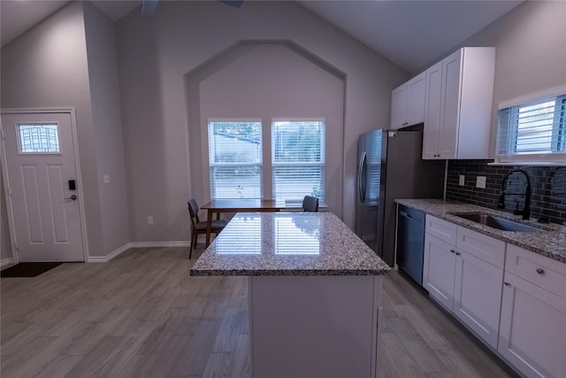 kitchen featuring white cabinetry, a center island, light stone countertops, stainless steel dishwasher, and sink