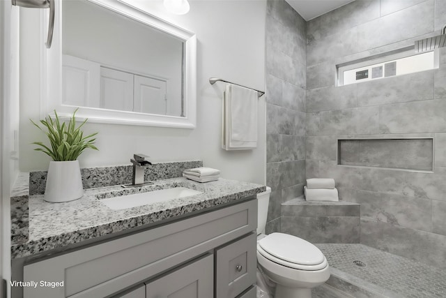 bathroom with toilet, vanity, and a tile shower