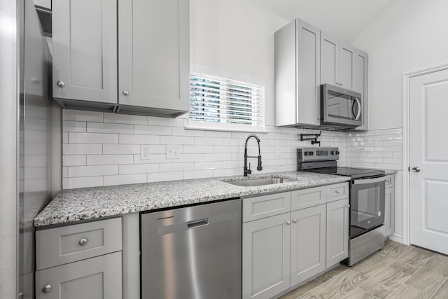 kitchen featuring stainless steel appliances, sink, gray cabinets, light stone counters, and light hardwood / wood-style flooring