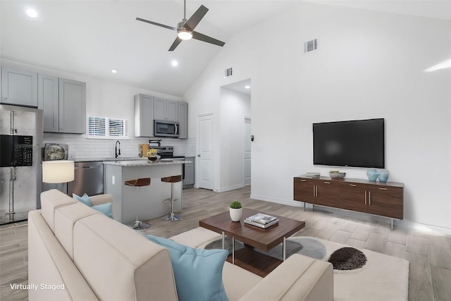 living room with ceiling fan, high vaulted ceiling, and light hardwood / wood-style flooring