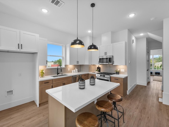 kitchen with stainless steel appliances, white cabinets, a kitchen island, and sink