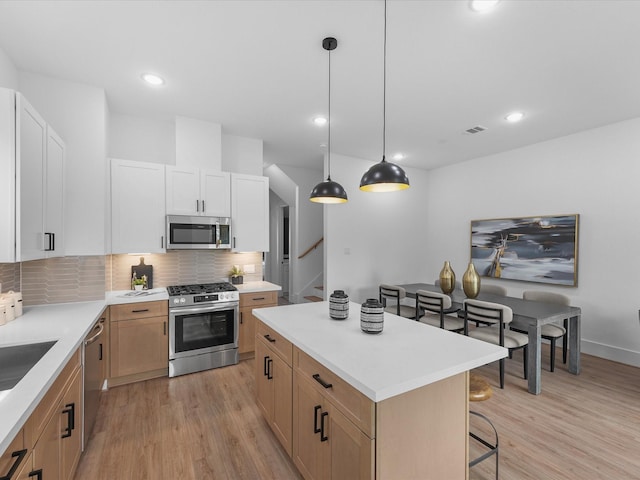 kitchen featuring appliances with stainless steel finishes, a center island, decorative light fixtures, white cabinetry, and tasteful backsplash