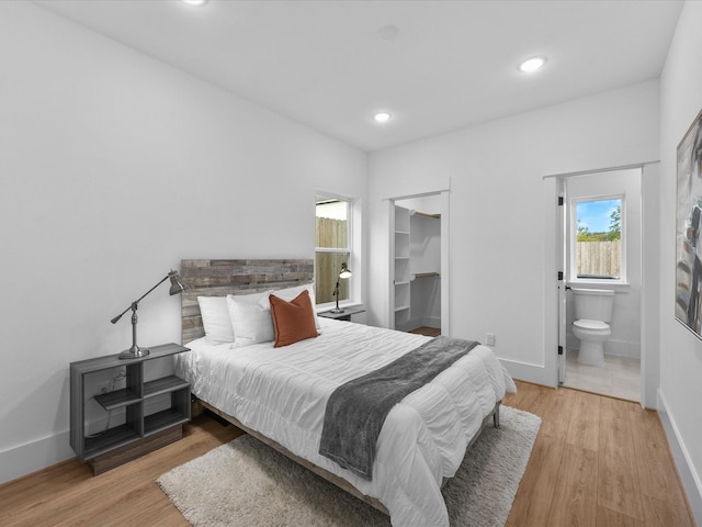 bedroom featuring a walk in closet, connected bathroom, and light hardwood / wood-style flooring