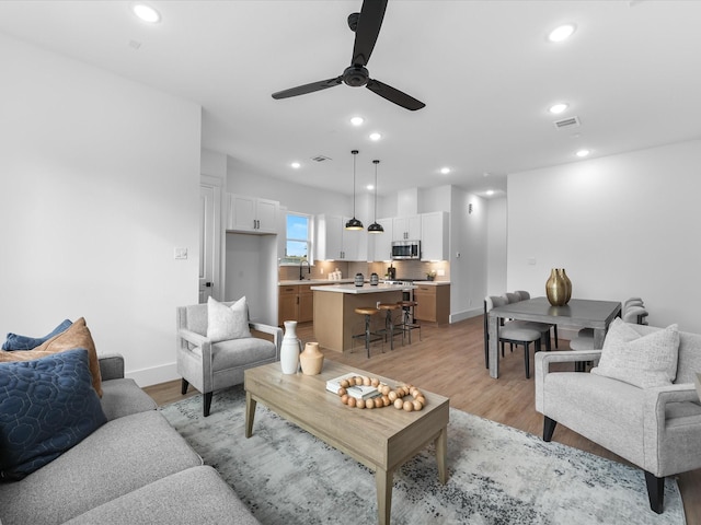 living room with light wood-type flooring, ceiling fan, and sink