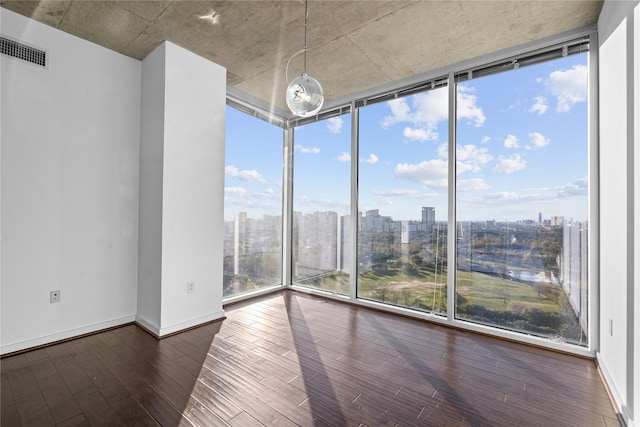 empty room featuring a wall of windows, dark hardwood / wood-style floors, and a healthy amount of sunlight