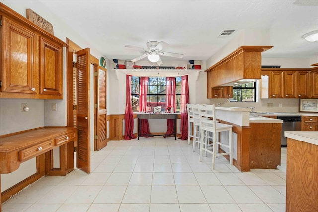 kitchen featuring a kitchen bar, kitchen peninsula, ceiling fan, stainless steel dishwasher, and sink