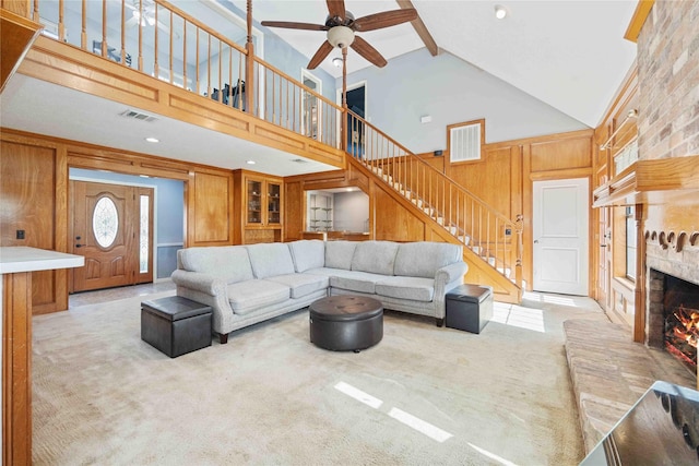 living room featuring beam ceiling, a large fireplace, wooden walls, light carpet, and high vaulted ceiling