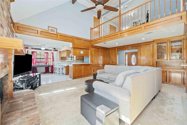 living room with light carpet, wooden walls, a stone fireplace, ceiling fan, and high vaulted ceiling