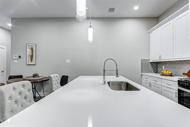 kitchen featuring white cabinets, gas stove, tasteful backsplash, sink, and hanging light fixtures