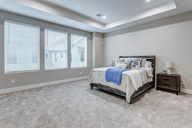 bedroom with light colored carpet and a tray ceiling