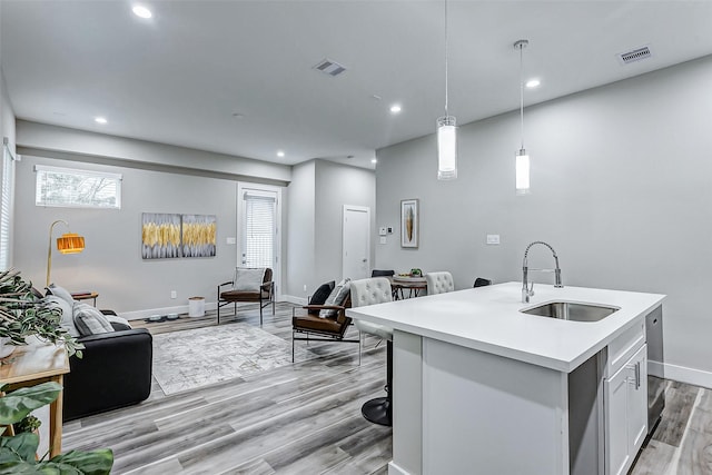 kitchen with decorative light fixtures, white cabinetry, light hardwood / wood-style floors, sink, and a kitchen island with sink