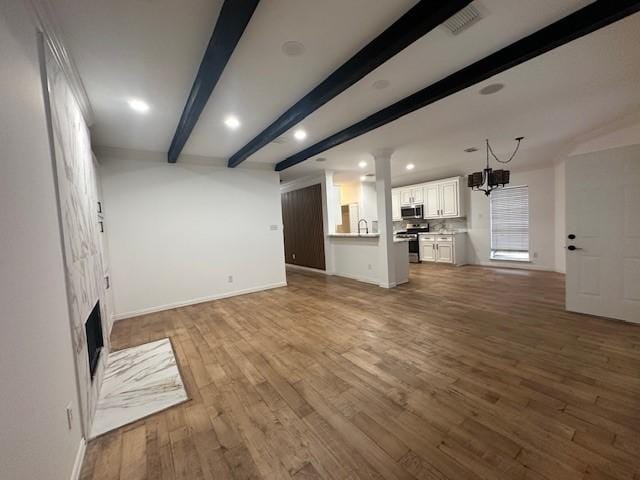 unfurnished living room featuring beamed ceiling, sink, a notable chandelier, hardwood / wood-style flooring, and decorative columns