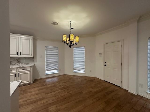 unfurnished dining area with dark hardwood / wood-style flooring, ornamental molding, and a notable chandelier