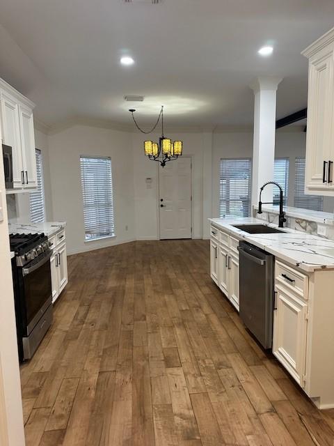 kitchen with hanging light fixtures, sink, white cabinetry, ornamental molding, and stainless steel appliances