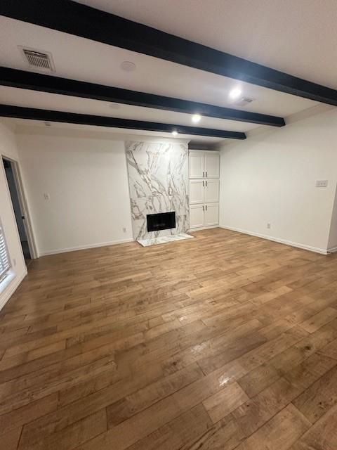 unfurnished living room with beamed ceiling, hardwood / wood-style floors, and a fireplace