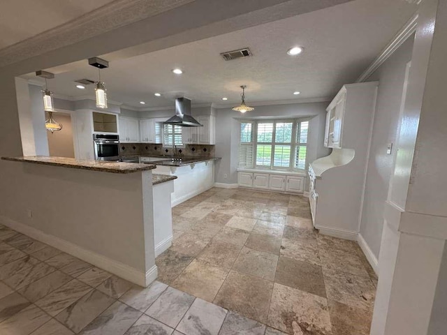 kitchen with dark stone countertops, oven, kitchen peninsula, white cabinetry, and island range hood