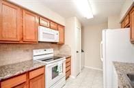 kitchen featuring decorative backsplash, light stone countertops, and white appliances