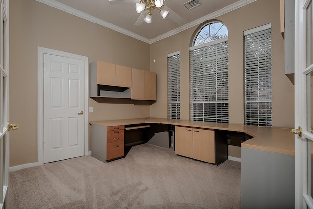 unfurnished office featuring crown molding, built in desk, light colored carpet, and ceiling fan