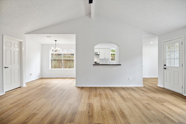 unfurnished living room featuring light wood-type flooring, a notable chandelier, plenty of natural light, and a textured ceiling