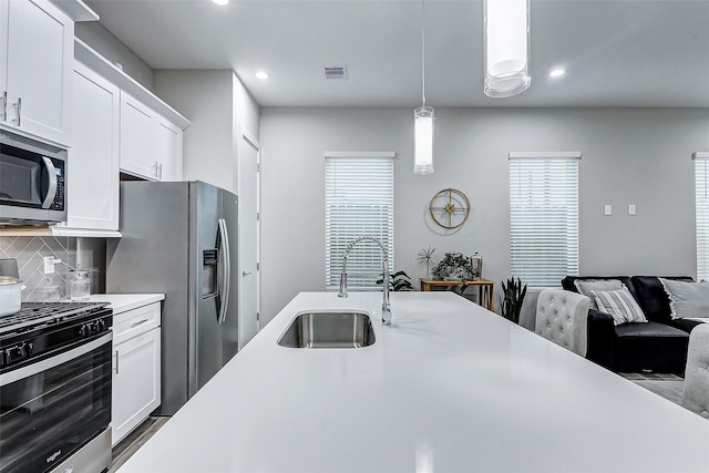 kitchen with appliances with stainless steel finishes, backsplash, pendant lighting, white cabinets, and sink