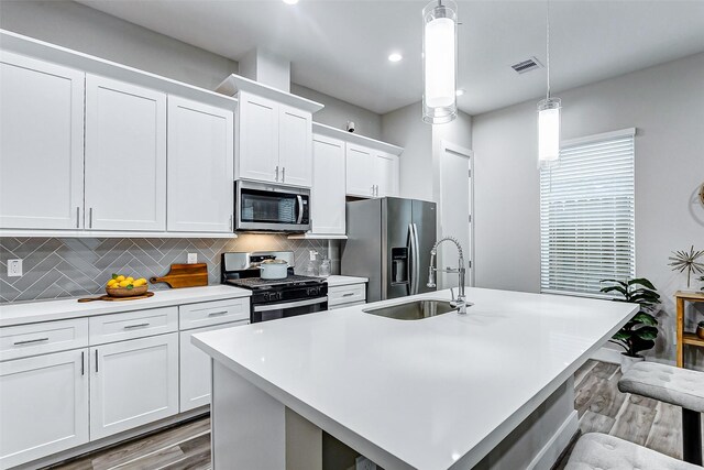 kitchen featuring pendant lighting, white cabinets, appliances with stainless steel finishes, sink, and a center island with sink