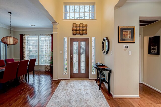 entryway with ornamental molding, wood-type flooring, and decorative columns