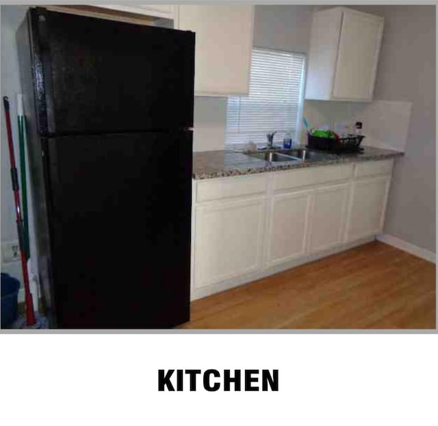 kitchen featuring light stone countertops, black refrigerator, white cabinetry, light hardwood / wood-style floors, and sink