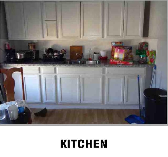 kitchen with sink, light hardwood / wood-style flooring, white cabinets, and light stone countertops