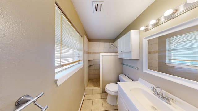 bathroom with toilet, vanity, tile patterned flooring, and a tile shower