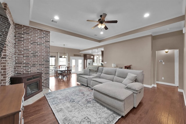 living room with ceiling fan, a fireplace, dark hardwood / wood-style flooring, and a raised ceiling