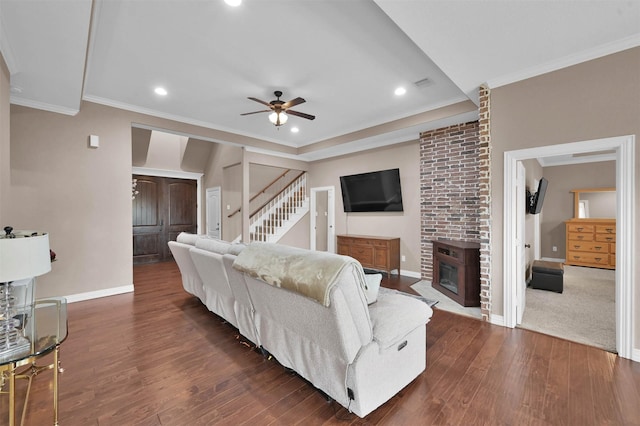 living room with a brick fireplace, dark hardwood / wood-style floors, crown molding, and ceiling fan