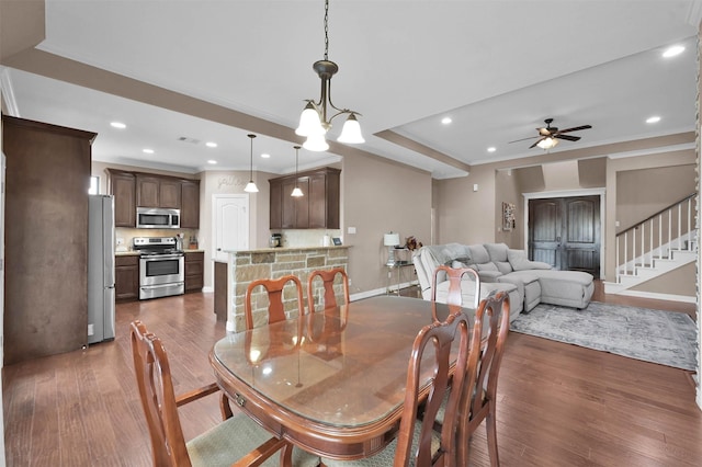 dining area with dark wood-type flooring, ornamental molding, and ceiling fan with notable chandelier