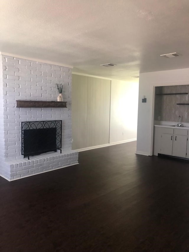 unfurnished living room with dark wood-type flooring, a brick fireplace, and sink