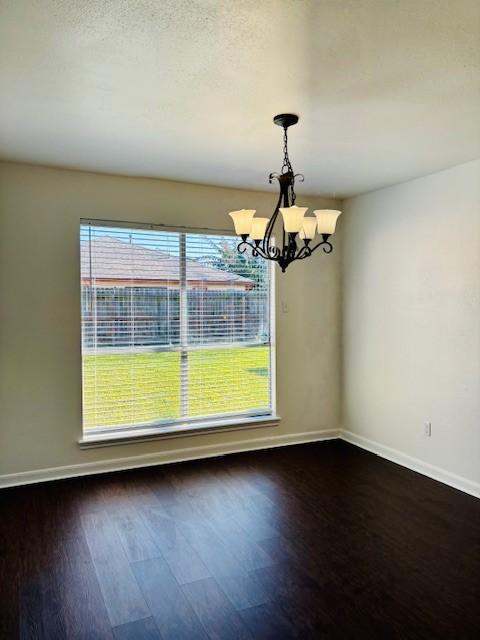 unfurnished dining area with dark wood-type flooring, a wealth of natural light, and an inviting chandelier