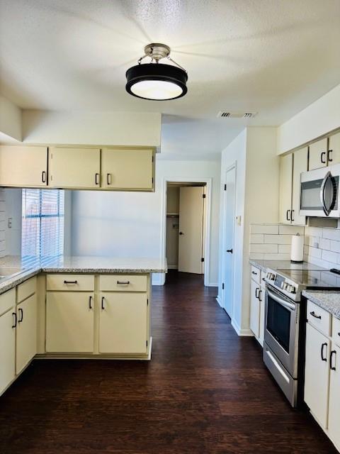 kitchen with decorative backsplash, kitchen peninsula, stainless steel appliances, and cream cabinetry